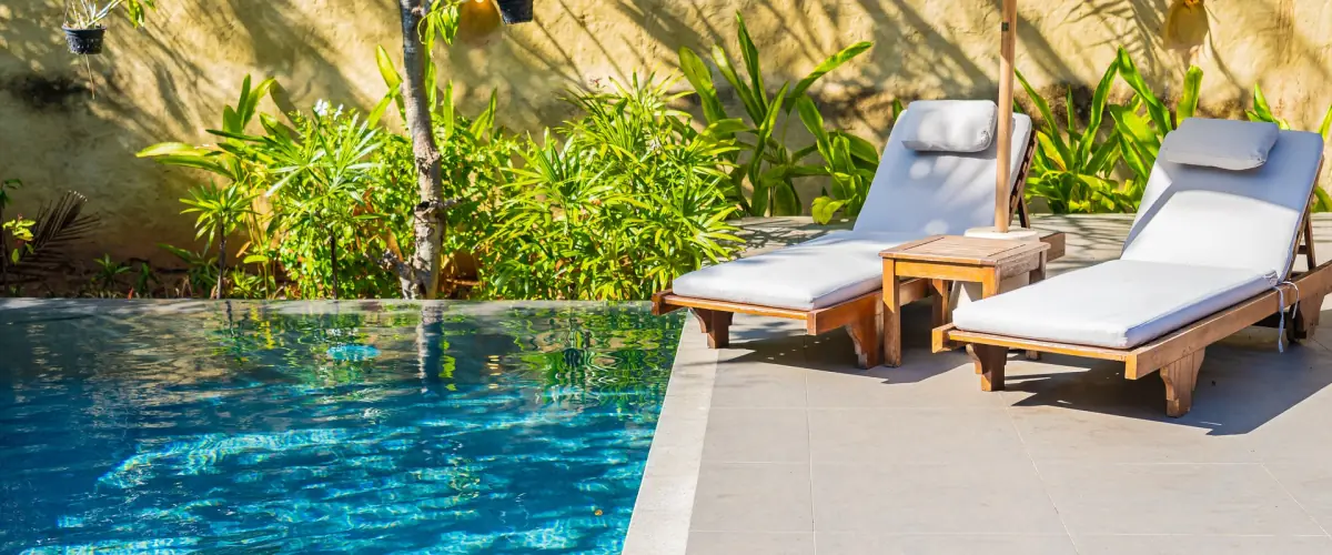 Teak lounger with white cushions at the edge of a pool